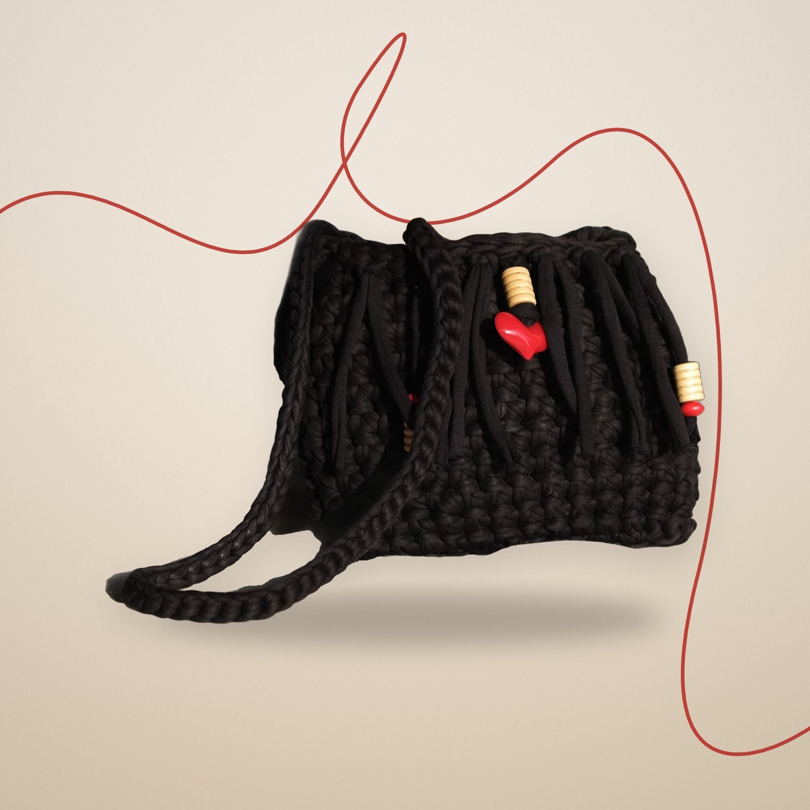 Borsa a tracolla nera all’uncinetto con frange, perline di legno e cuore rosso, vista di tre quarti